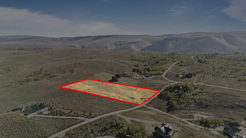 Expansive lot featuring a natural, undeveloped landscape with scattered vegetation, surrounded by rolling hills and distant mountains