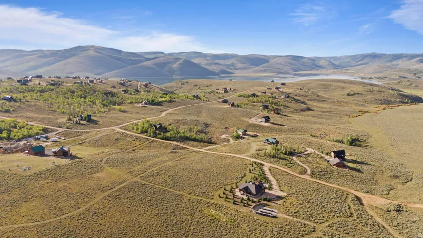 Expansive landscape featuring rolling hills and distant mountains, with scattered residences and a visible body of water