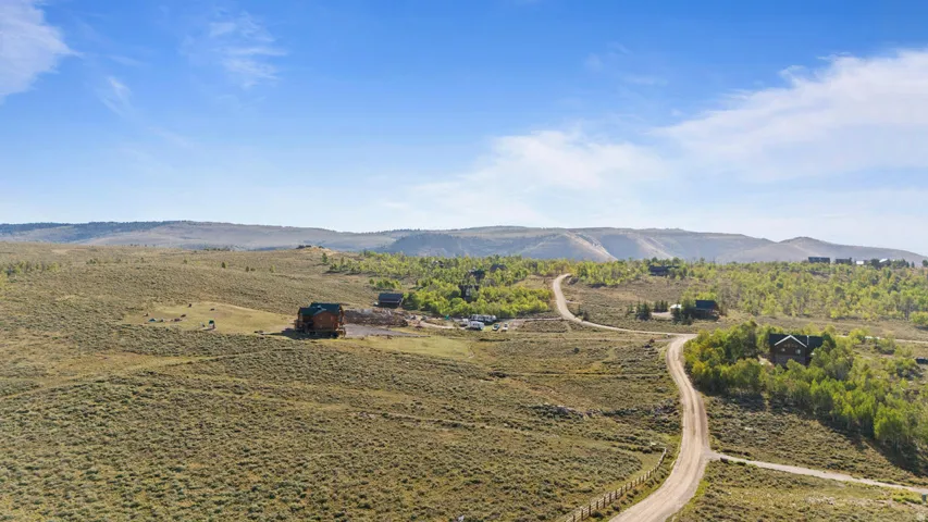 Expansive rural landscape with a winding unpaved road, scattered residential structures, and distant mountains