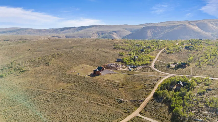 Expansive rural landscape featuring scattered residential structures, unpaved roads, and distant mountain ranges