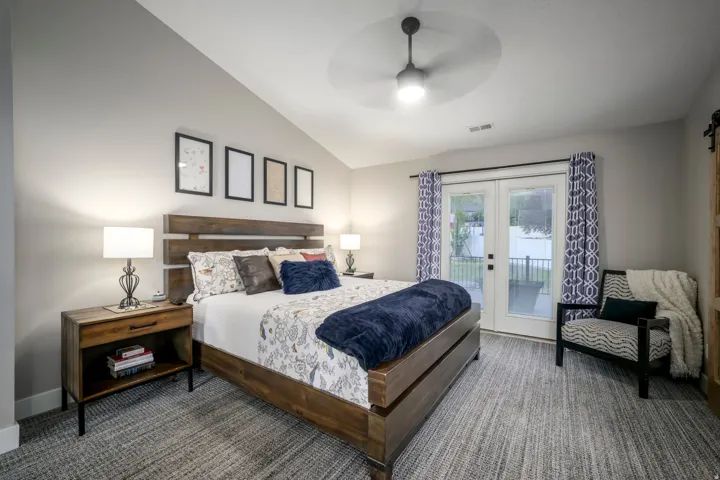Vaulted ceiling, ceiling fan with integrated lighting, double French doors, wood-finish flooring, and a sliding barn door