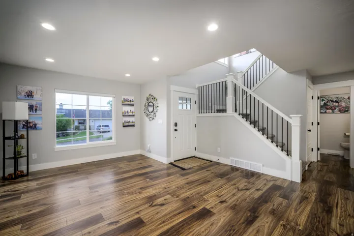 Wood-finish flooring throughout, white trim, recessed ceiling lighting, a staircase with black metal balusters, and a front entry door with integrated lites