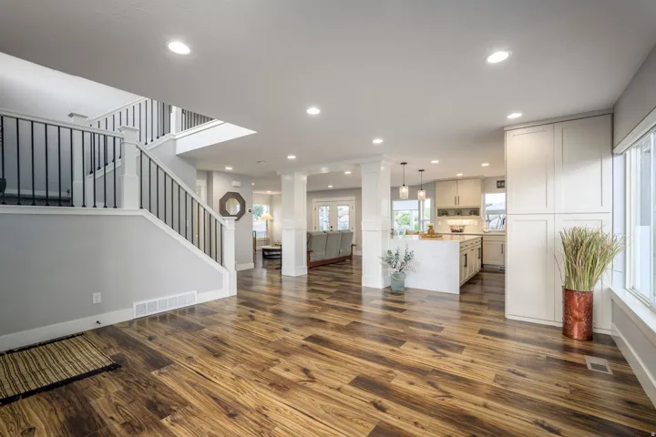 Wood-finish flooring, staircase with white newel posts and black balusters, recessed lighting, white kitchen cabinetry, and white kitchen island with pendant lighting