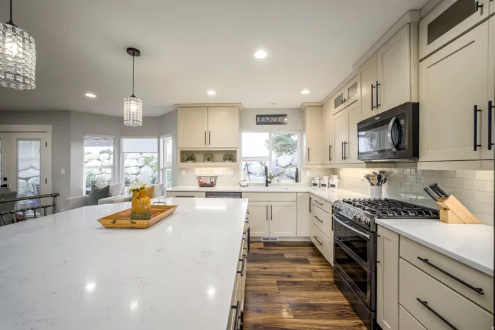 Kitchen featuring an expansive island with a light-toned countertop, wood-finish flooring, light-toned cabinetry with dark hardware, a gas range, and a tile backsplash