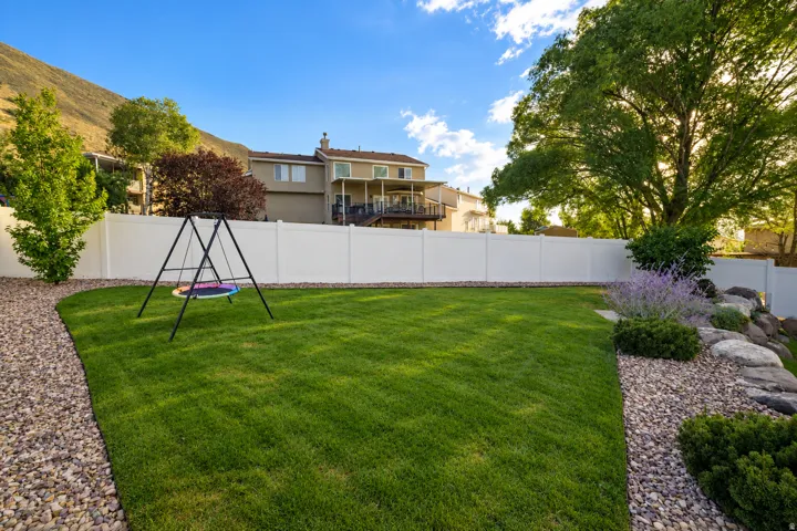 Expansive backyard with a manicured lawn, a gravel pathway, and a white privacy fence