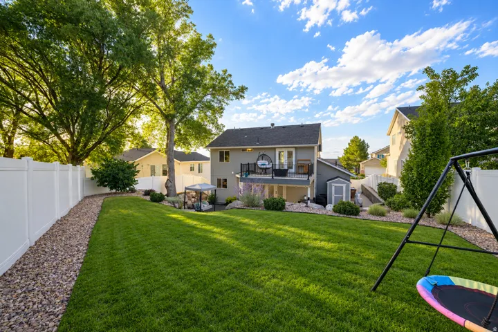 Expansive backyard featuring a manicured lawn, established trees, white privacy fencing, and a gravel border