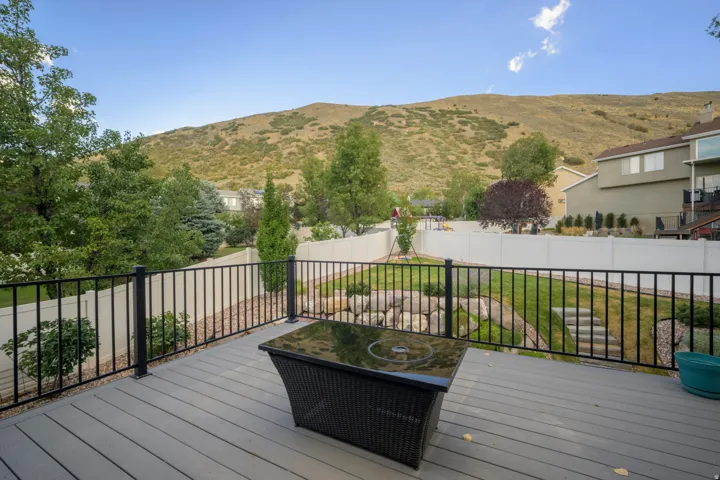Expansive backyard featuring a composite deck, black metal railings, a manicured lawn, and natural rock landscaping