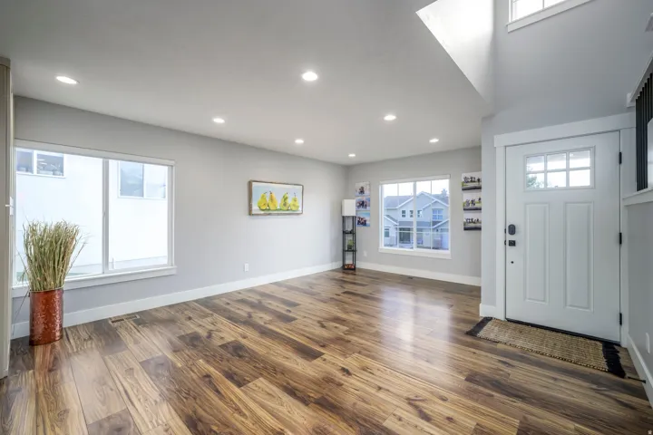 Wood-finish flooring, recessed lighting, multiple windows, a white paneled entry door with window panes, and a high ceiling