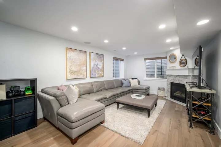 Recessed lighting, wood-finish flooring, corner fireplace with stone surround, two windows with blinds, and built-in shelving