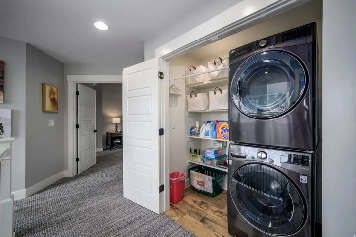 Laundry closet with stackable washer and dryer, adjacent to a hallway with patterned carpet flooring