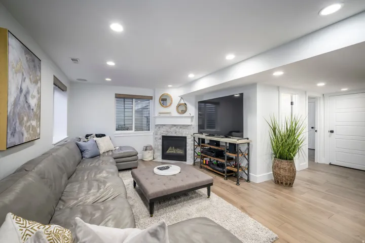 Recessed lighting, wood-finish flooring, and a stone-surround fireplace with a white mantel
