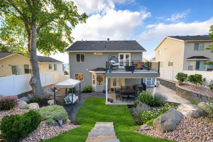 Multi-level backyard featuring a manicured lawn, stone steps, and a built-in elevated deck with black railing