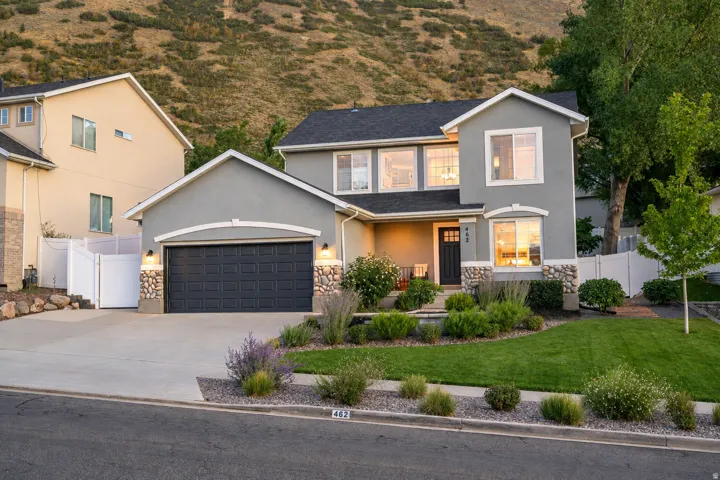 Stucco exterior with stone accents, attached two-car garage, manicured front lawn, and mature landscaping