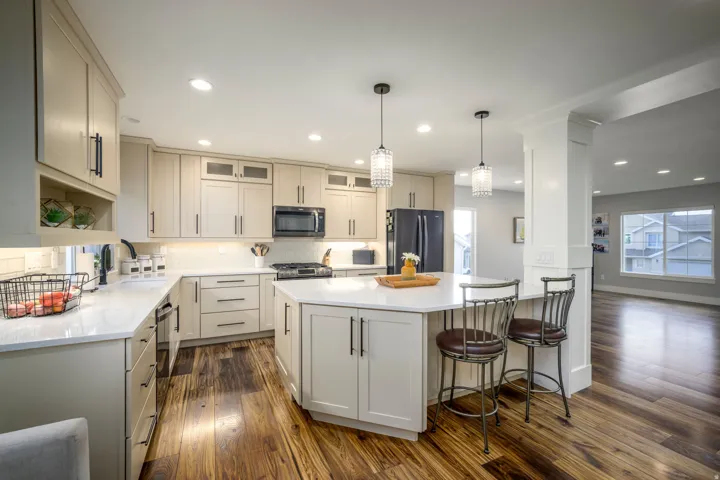 Kitchen featuring light-toned cabinetry, a central island with countertop seating, stainless steel appliances, and wood-finish flooring