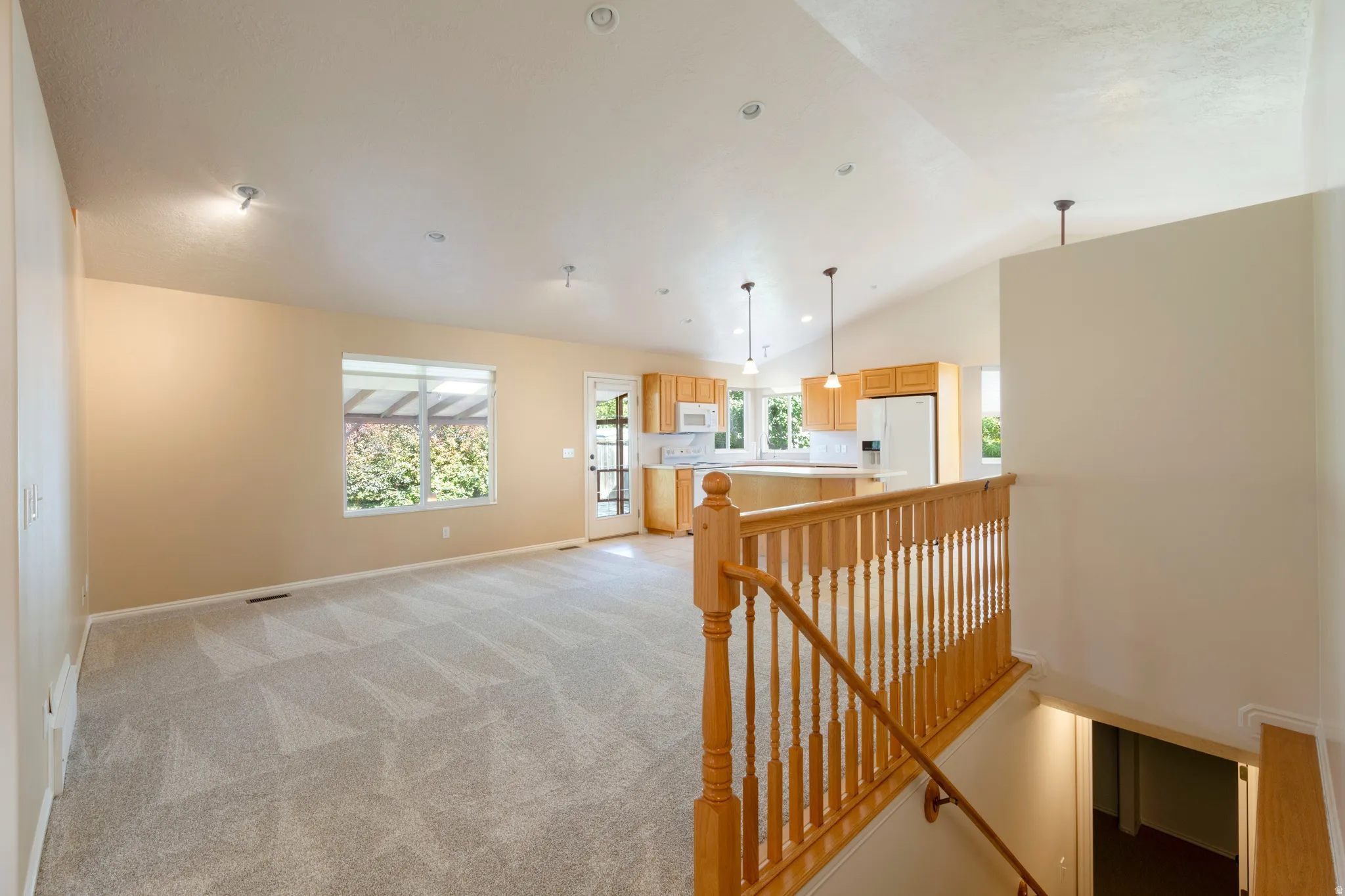 Vaulted ceiling, recessed lighting, light wood-finish stair railing, and a window with exterior landscaping