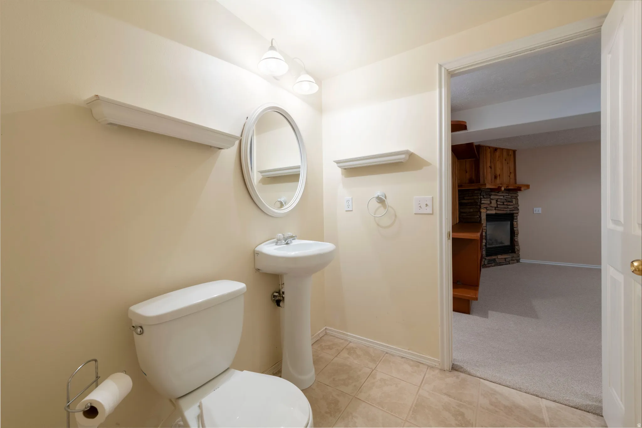 Pedestal sink with an oval mirror, overhead vanity lighting, and ceramic tile flooring