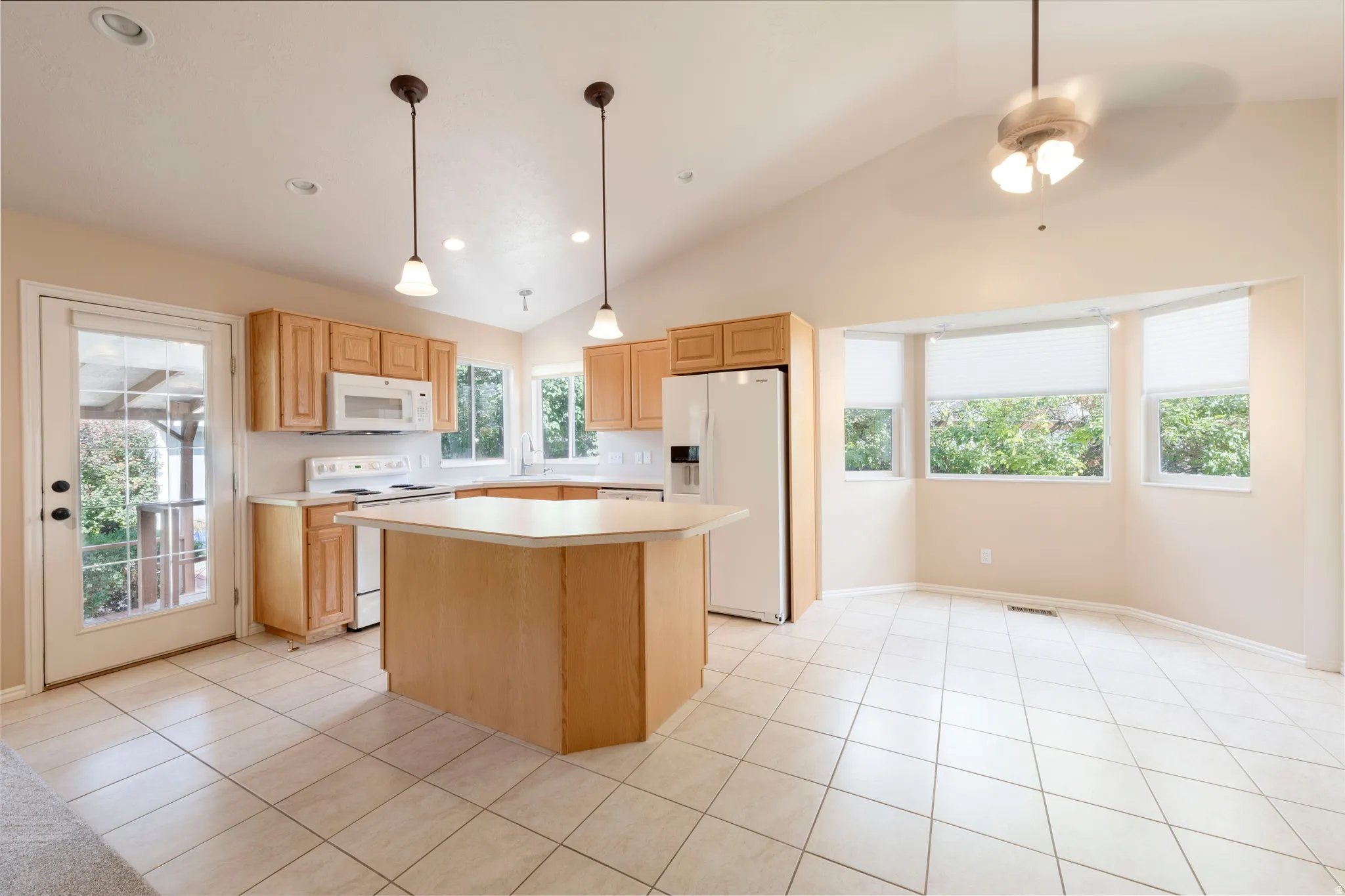 Kitchen featuring light wood cabinetry, white appliances, a center island with countertop, and tiled flooring