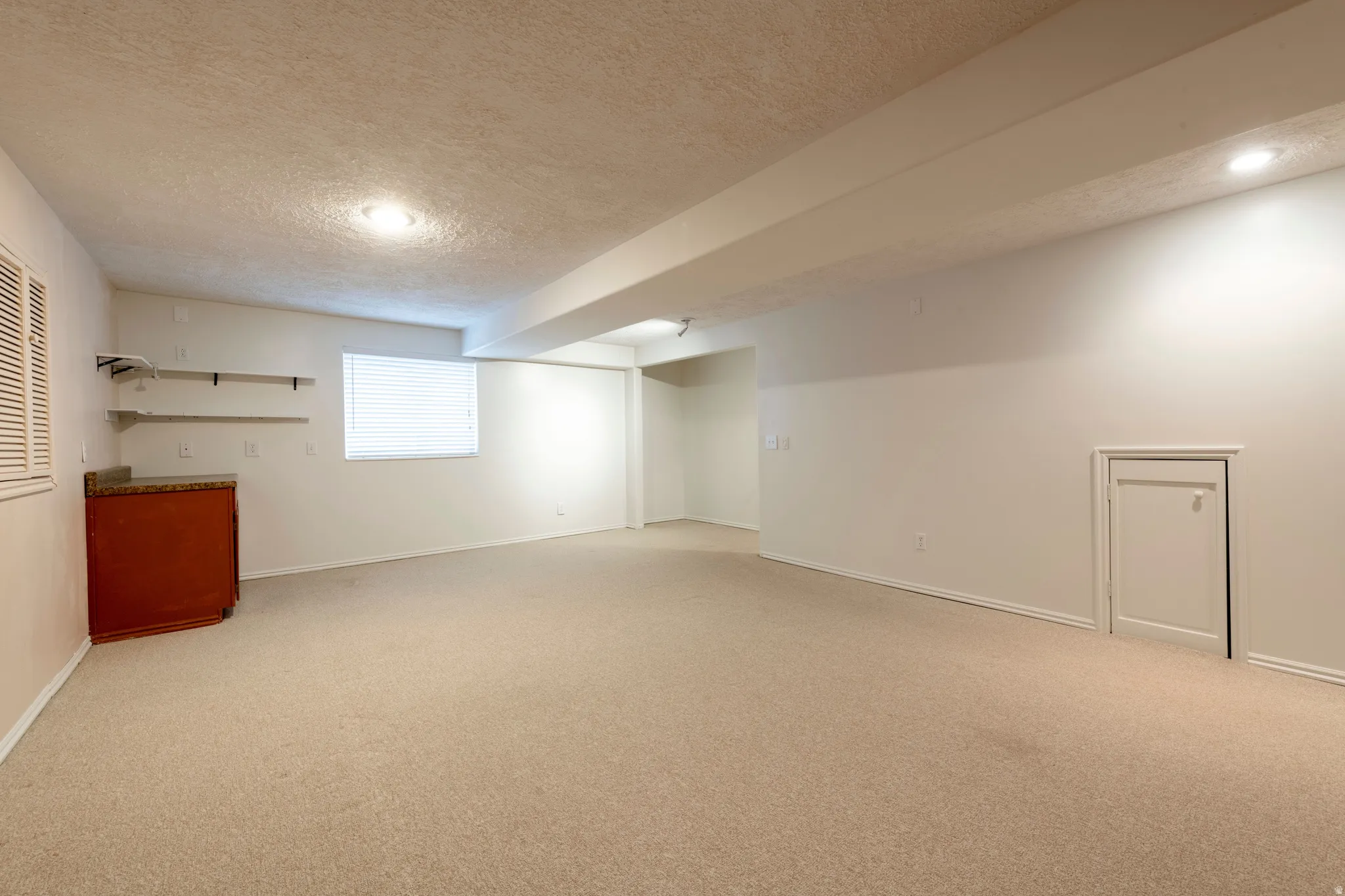 Spacious room featuring neutral carpeting, recessed lighting, a built-in cabinet with a stone-finish countertop, and open shelving