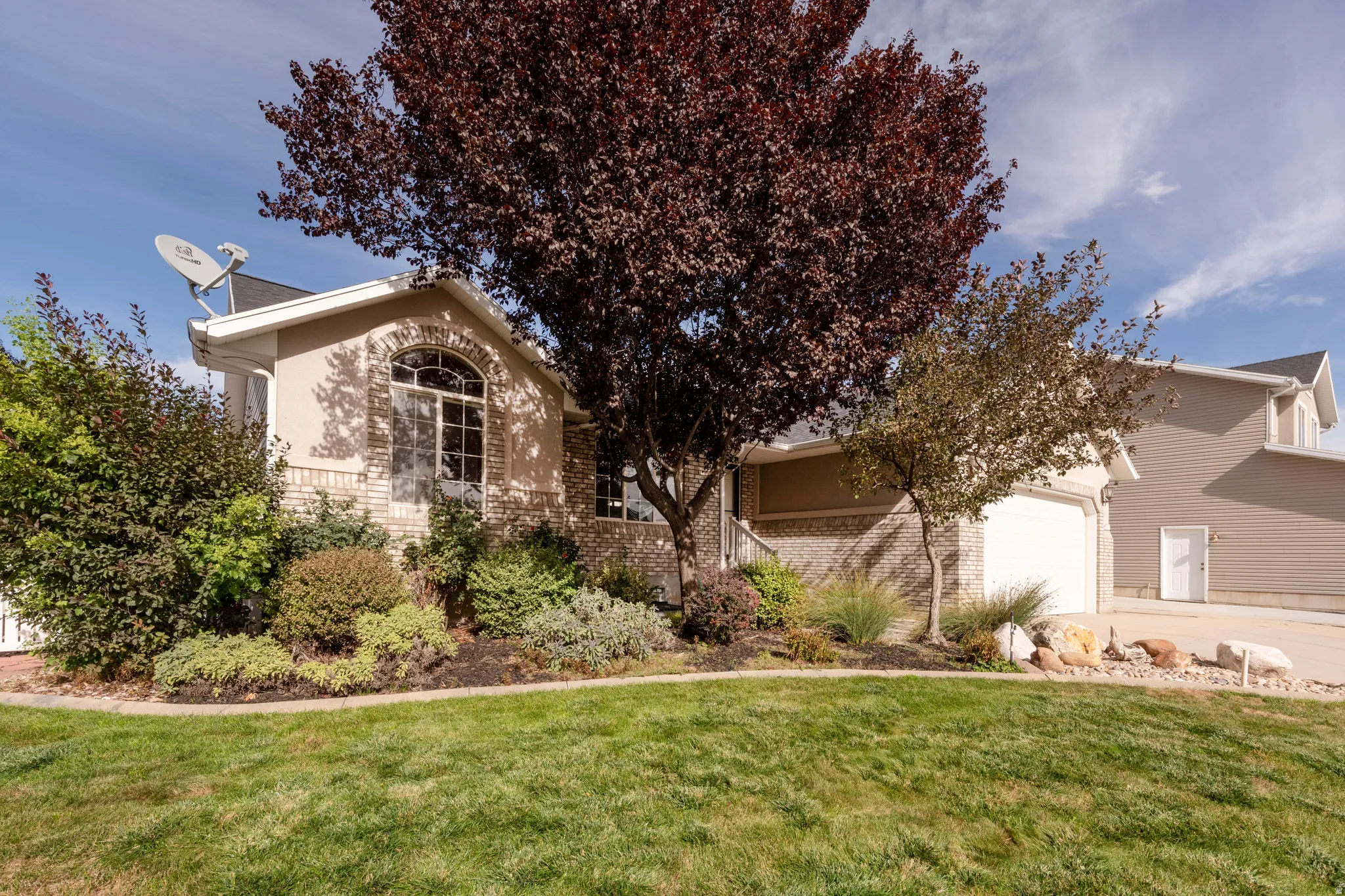 Stucco exterior with brick detailing, arched window, attached garage, and mature landscaping