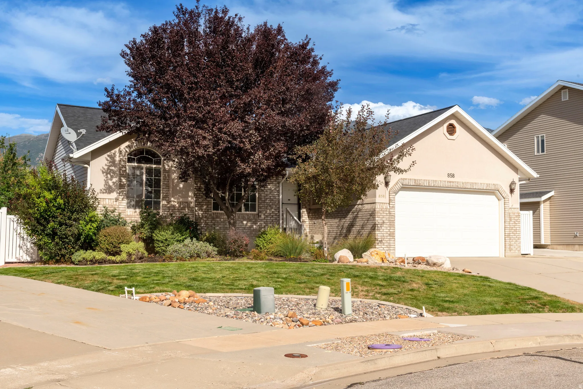 Stucco and brick facade with an attached two-car garage, mature landscaping, and a manicured lawn