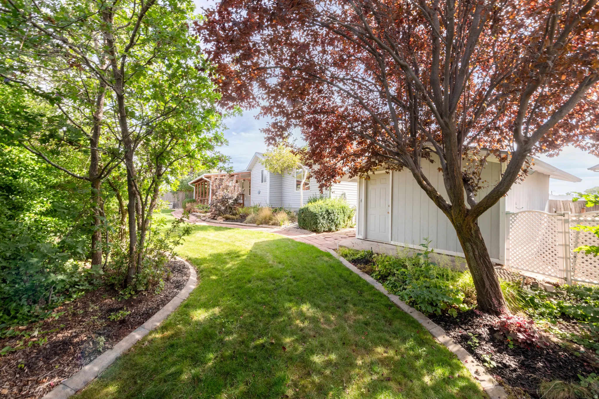Manicured lawn with concrete curbing, mature trees, landscaped planting beds, and a white storage shed