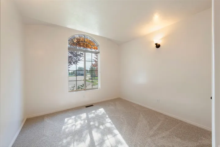 Arched window with gridded upper pane, wall-mounted sconce, and neutral carpeting