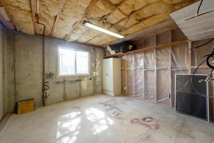 Concrete floor and walls, exposed ceiling joists with insulation, fluorescent overhead lighting, and a single window