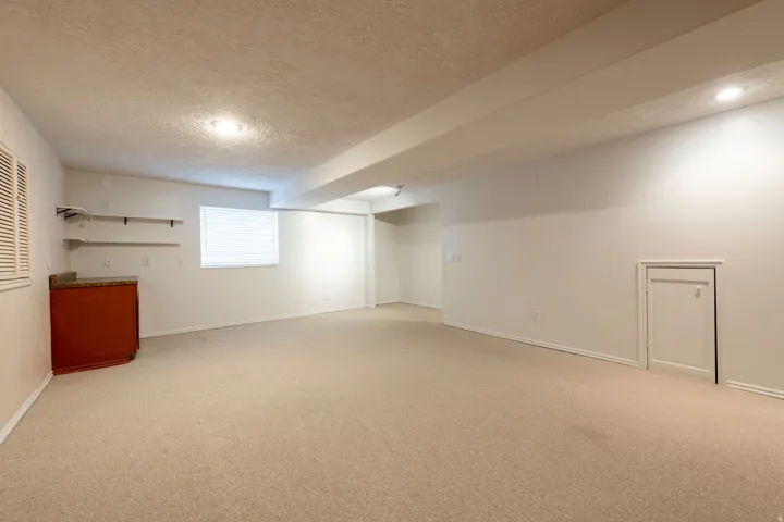 Spacious room featuring neutral carpeting, recessed lighting, a built-in cabinet with a stone-finish countertop, and open shelving