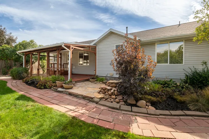 Covered deck, flagstone patio, brick paver pathway, rock landscaping, and mature plantings