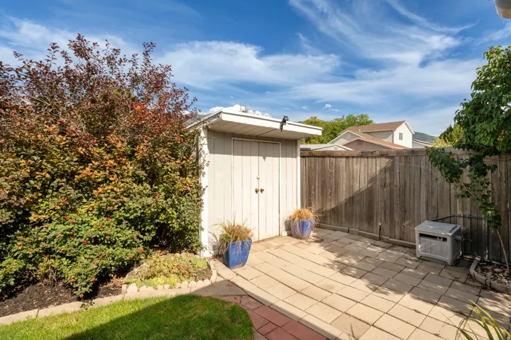 Storage shed, paved patio, wood privacy fencing, mature landscaping, and green lawn
