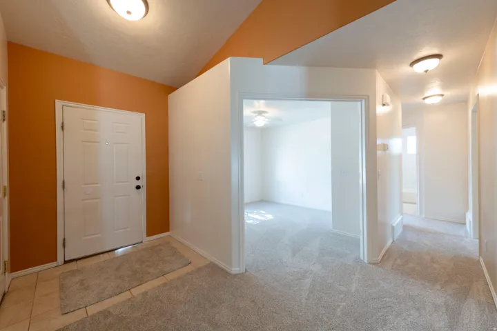 Tiled entryway with a paneled door, leading to carpeted areas with flush-mount lighting and a ceiling fan in the adjacent room