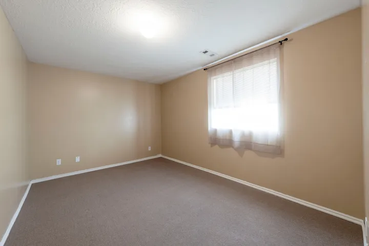 Carpeted room with neutral-toned walls, a single window, and overhead lighting