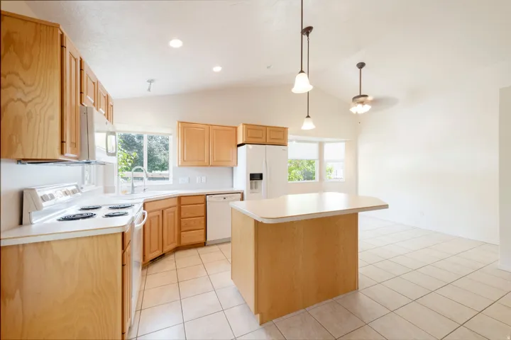 Kitchen featuring wood cabinetry, white appliances, a center island with counter seating, and tile flooring