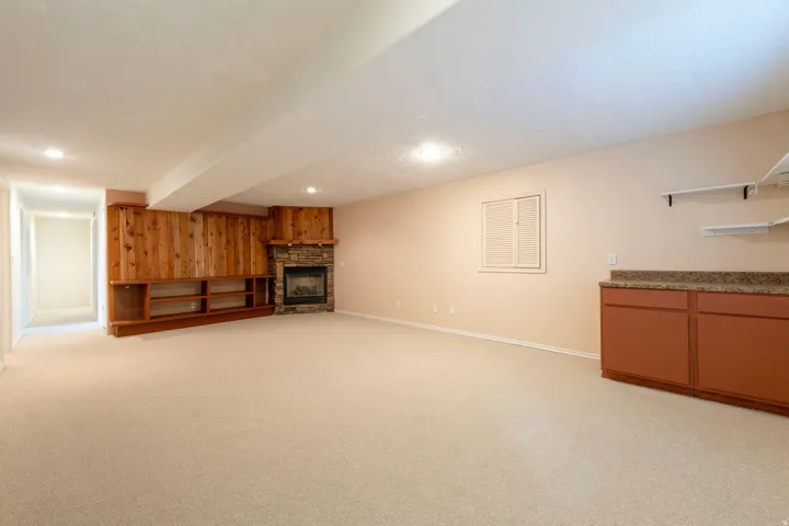 Spacious finished room featuring a stone-clad corner fireplace, built-in wood shelving, recessed lighting, and a built-in counter with cabinetry