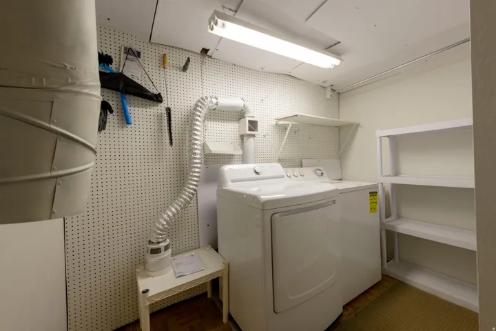 Laundry area featuring a washer and dryer, pegboard wall, overhead fluorescent lighting, and built-in shelving