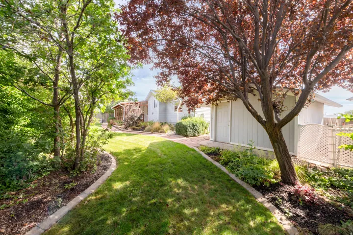 Manicured lawn with concrete curbing, mature trees, landscaped planting beds, and a white storage shed