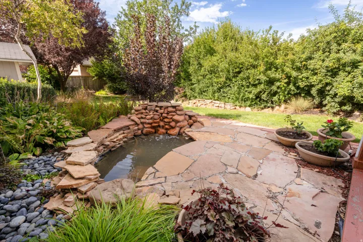 Landscaped backyard featuring a flagstone patio, rock-lined pond, and mature plantings