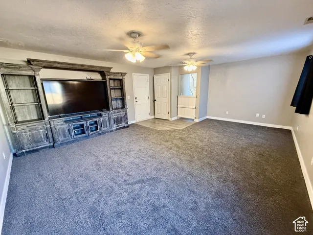 Expansive room featuring dark carpet flooring, a built-in entertainment center with shelving, and ceiling fans