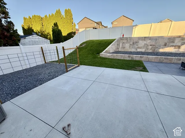 Expansive concrete patio with a stone retaining wall, terraced landscaping, and a fenced gravel area
