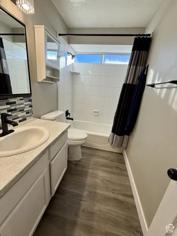 White tile bath/shower combination with a single basin vanity, light-toned countertop, and wood-finish flooring