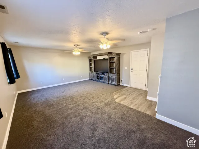 Spacious living area featuring neutral-toned walls, two ceiling fans, and a built-in media console
