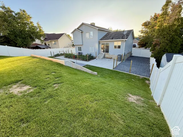Backyard featuring a sloped lawn, concrete patio, and a gravel pad