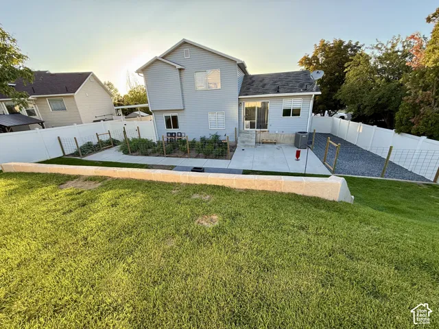 Expansive backyard featuring a concrete patio, white vinyl fencing, a gravel area, and a retaining wall