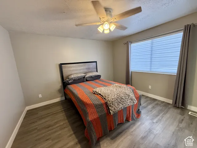 Wood-finish flooring, ceiling fan with integrated lighting, window treatments, and neutral wall tones