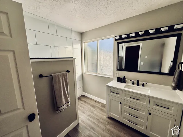 White subway tile shower enclosure, light-toned wood-finish flooring, white vanity with integrated sink, black framed mirror, and a multi-bulb vanity light fixture
