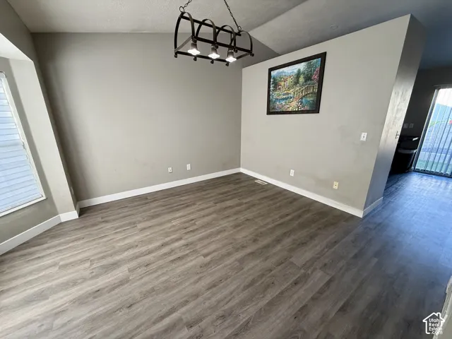Vaulted ceiling with a wrought iron chandelier, wood-finish flooring, and a large window with horizontal blinds