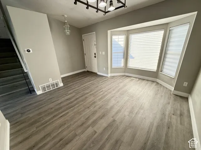 Bay window with multiple panels, wood-finish flooring, entry door, staircase, and a contemporary chandelier