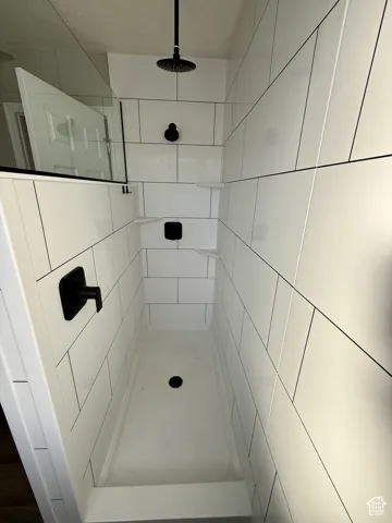 Walk-in shower with subway tile walls, built-in shelving, matte black fixtures, and a glass partition