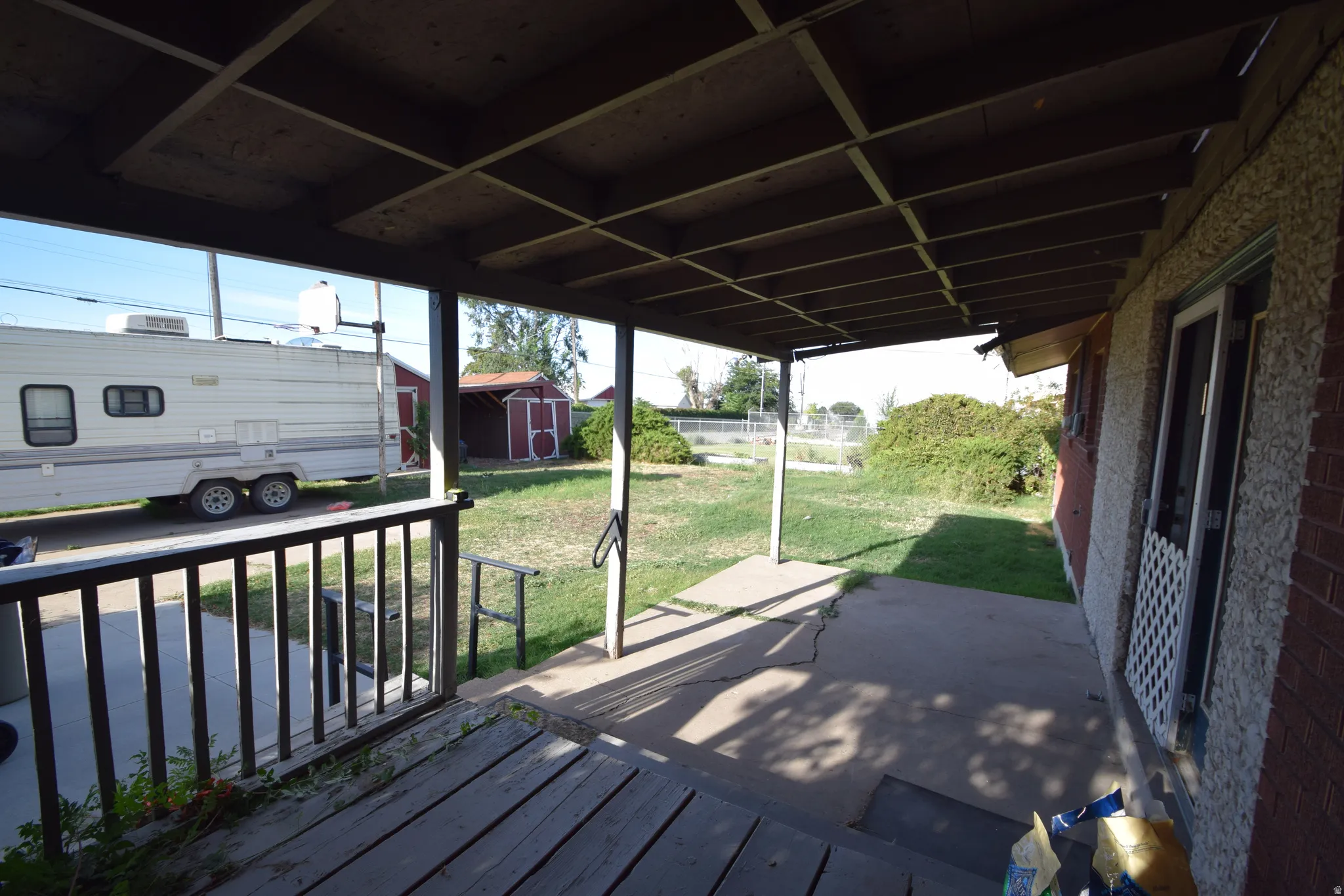 Covered patio with a concrete slab, wood deck, and a wooden railing