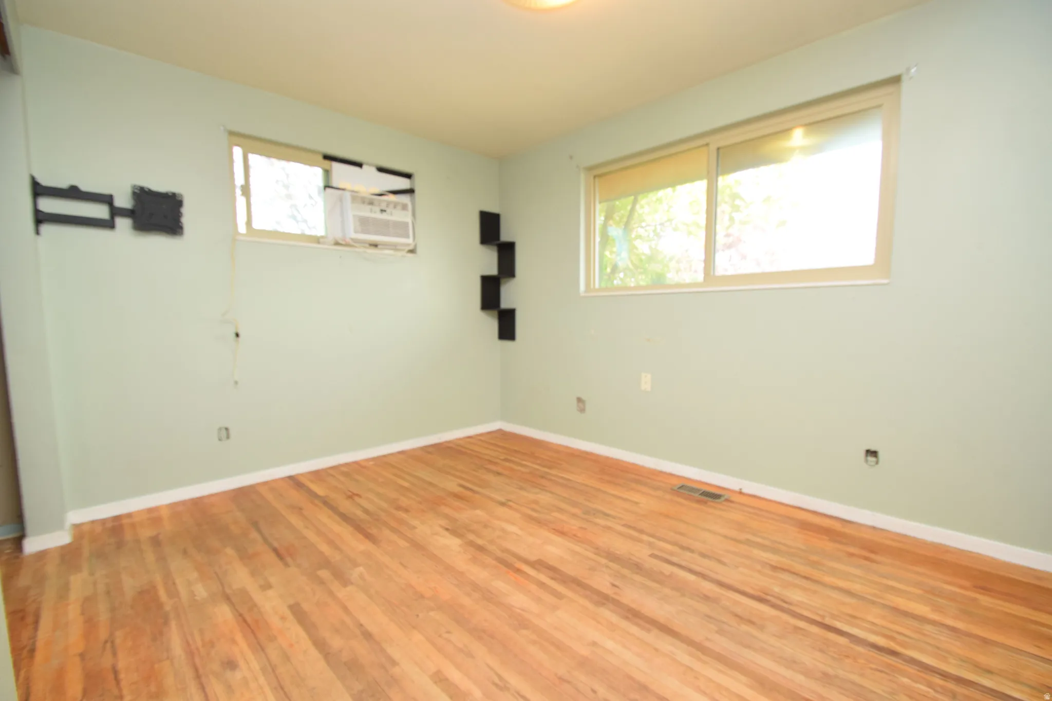 Hardwood flooring, multiple windows providing natural light, and a built-in wall-mounted air conditioning unit